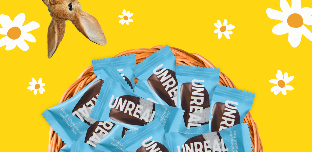 Basket of blue-wrapped UNREAL dark chocolate coconut bar on yellow background with daisies and rabbit ear