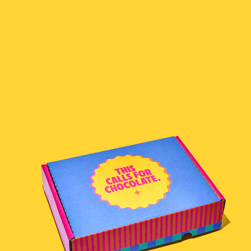 Angled view of Unreal Gift Box with This calls for chocolate printed on the blue lid, pink striped sides, yellow background