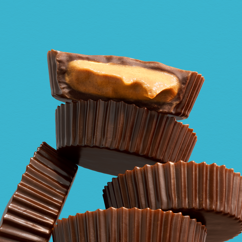 Stack of chocolate peanut-butter cups, one sliced open to reveal creamy peanut butter filling on a teal background.