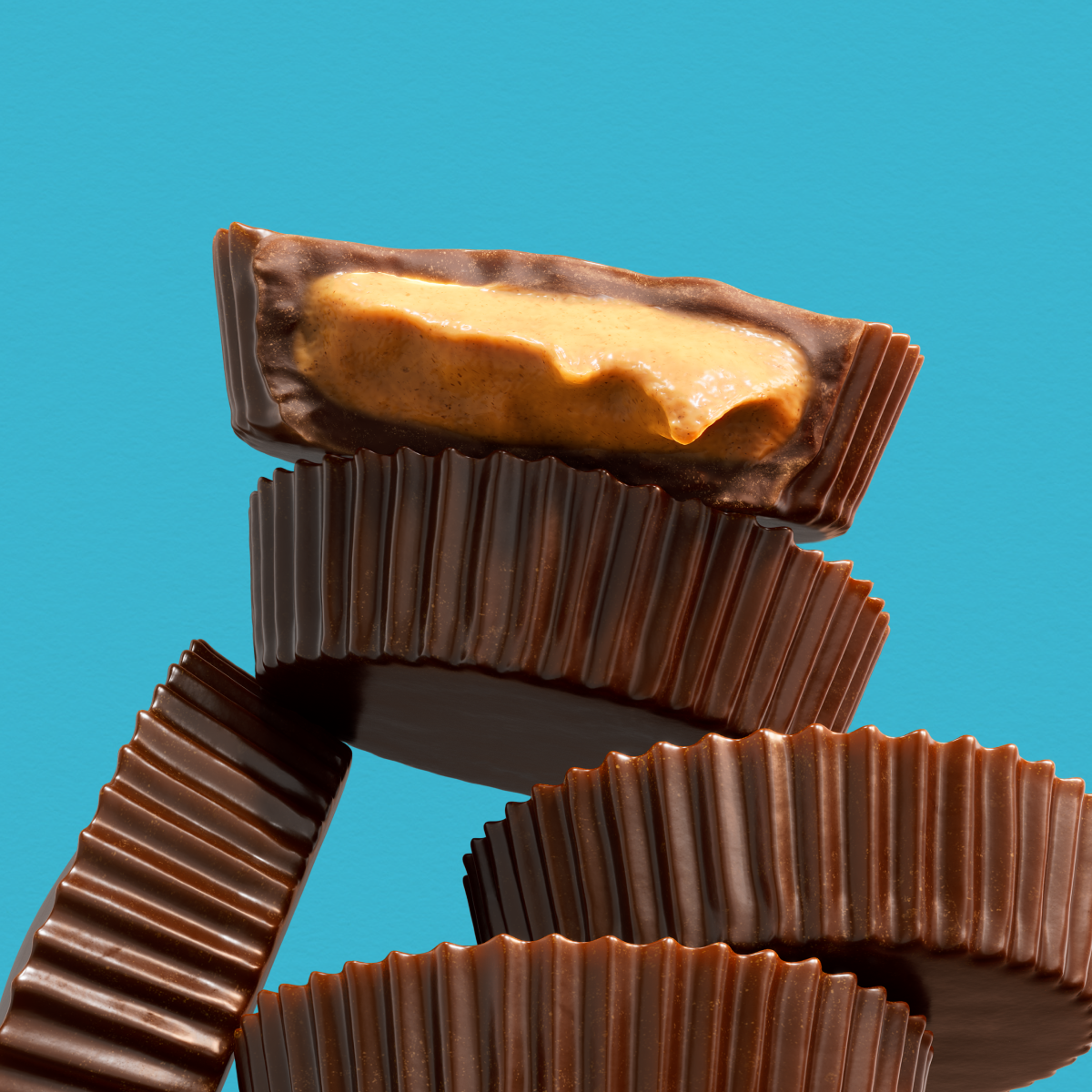 Stack of chocolate peanut-butter cups, one sliced open to reveal creamy peanut butter filling on a teal background.