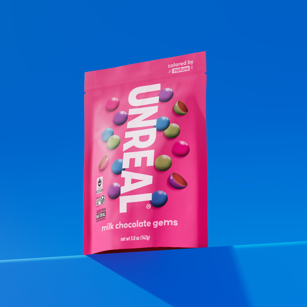 UNREAL milk chocolate gems package with colorful candy pieces and text including 'colored by nature', 'milk chocolate gems', and 'net wt 5.0 oz (142g)'
