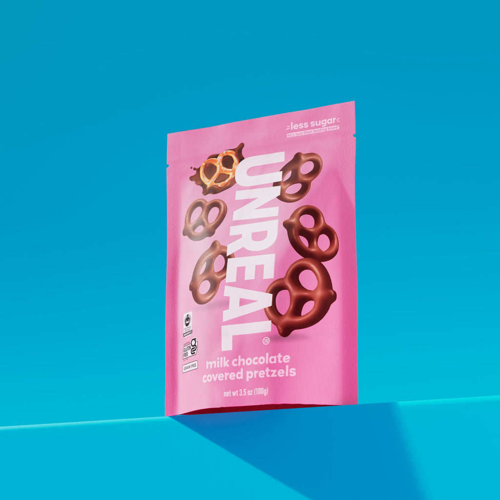 Pink package of Unreal milk chocolate covered pretzels with text less sugar, gluten free, grain free