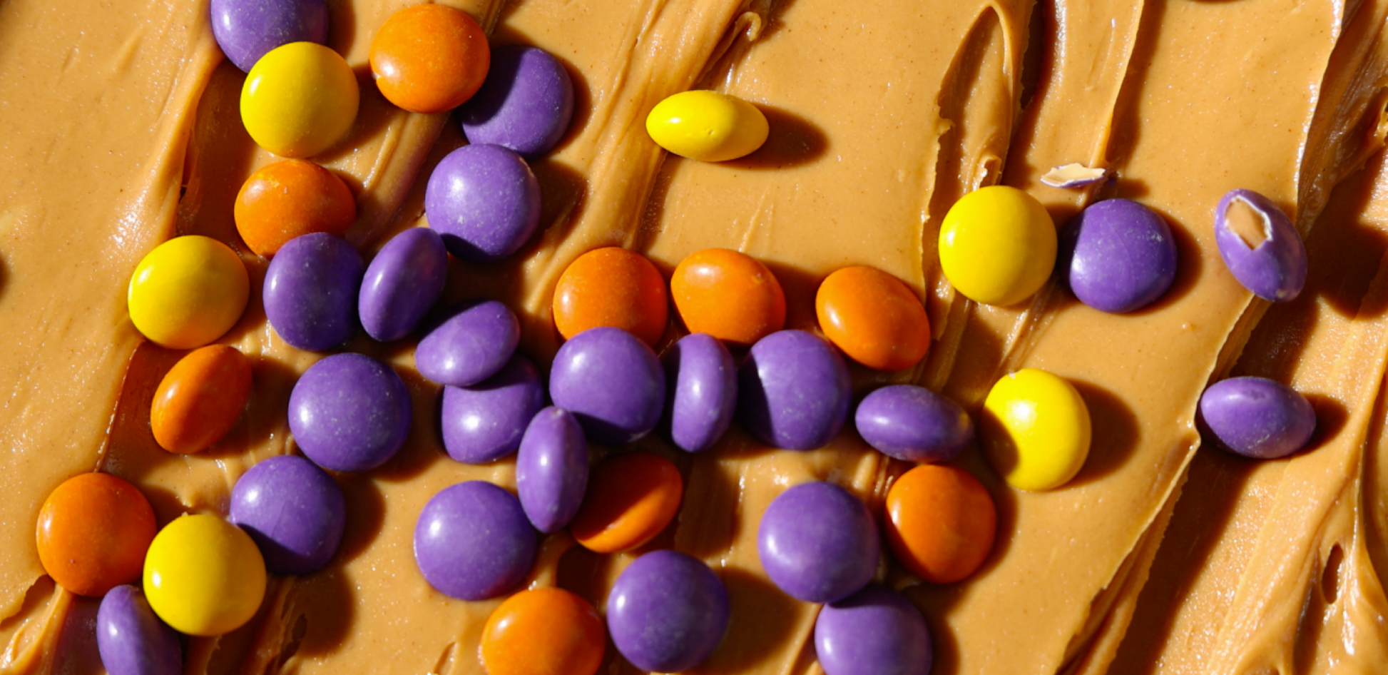 Close-up of Peanut Butter Drops showing purple, orange, and yellow candy-coated pieces on swirled peanut butter