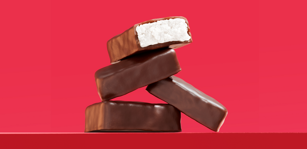 Stacked chocolate-covered coconut bars on red background, top bar cut to show white coconut filling.