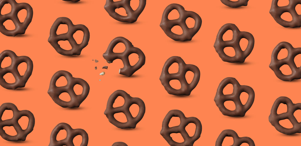 Chocolate-covered pretzels on an orange background, one partially eaten with crumbs visible